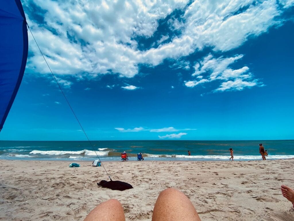 A serene view of Kure Beach, NC, with the ocean and blue sky seen from under a Shibumi shade, capturing a relaxing beach day.