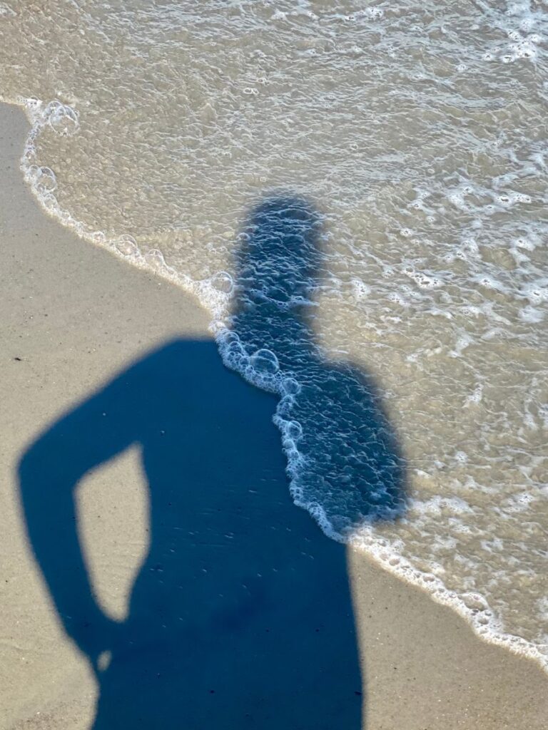 A silhouette of a person reflected in the wet sand as gentle waves wash onto the beach at Kure Beach, NC.